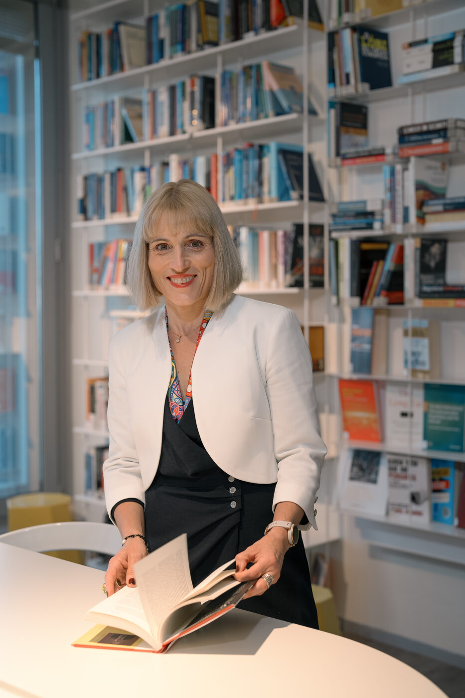 Retrato corporativo de mulher com livro em biblioteca, fotografia editorial para revista
