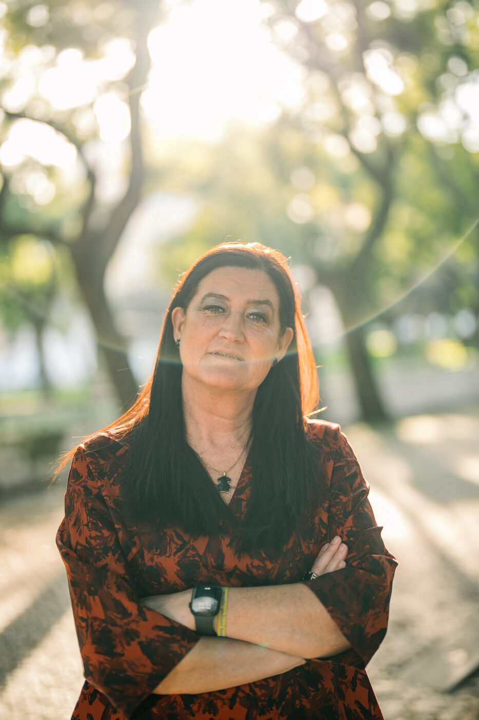 Retrato corporativo de mulher de braços cruzados em exterior com contraluz, fotografia profissional