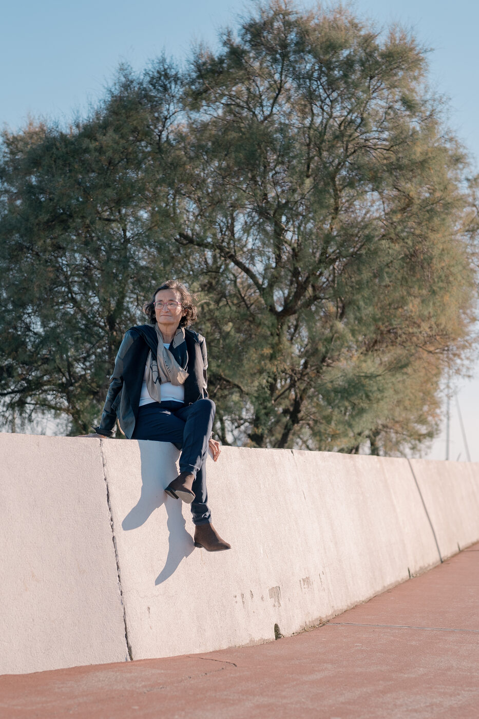 Retrato de mulher sentada num muro junto a uma árvore, fotografia profissional em exterior com luz natural