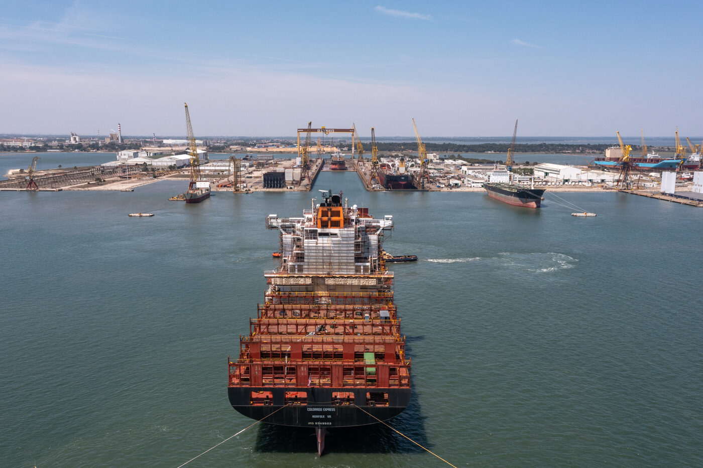 Worker walking beside a ship's bulbous bow in dry dock, showing the scale of the retrofit at Lisnave, Setúbal